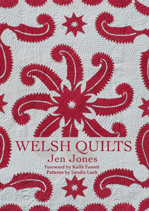 This cover shows a light grey background with a red pattern quilted on. The Text reads: Welsh Quilts. Jen Jones. Foreword by Kaffe Fassett. Patterns by Sandie Lush.