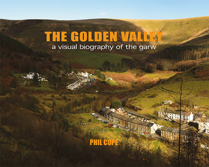 This cover shows a photograph of the Garw Valley. There are hills in the background which are illuminated by sunshine. Below the hills is a small village. The text reads: The Golden Valley: A Visual Biography of the Garw. By Phil Cope.