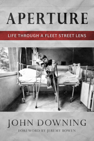 This cover shows a black and white photograph of a boy sat alone on a hospital bed. One of his legs is missing from the knee down and he is resting on crutches. The text reads: Aperture: Life Through a Fleet Street Lens. John Downing.