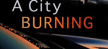 This cover shows a fiery sunset over a city scape reflected in the bonnet of a car. The text reads: A City Burning. Angela Graham.