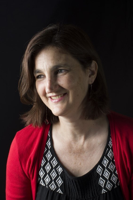 Cath Drake is a white woman with short dark hair. She is wearing a black top and red cardigan.