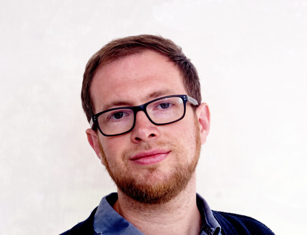 Photo of Dai George. He is wearing a blue shirt and dark rimmed glasses.