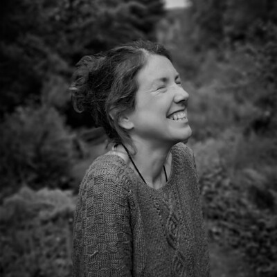 Black and white photo of Julie Brominicks. She is standing outside and is turned slightly away from the camera laughing with her eyes closed.