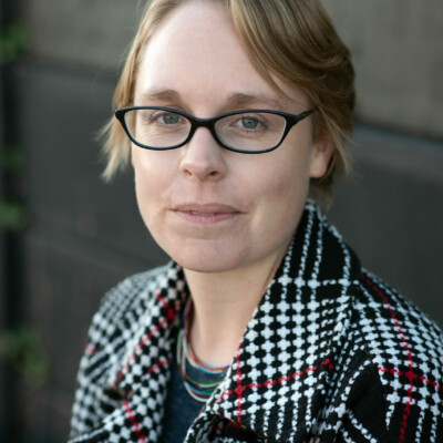 Katherine Stansfield is white woman with short blonde hair which stops past her ears. She is wearing glasses and looking at the camera. She is wearing a dark coat with a white pattern on the collar.
