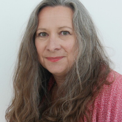 Kate Noakes is a white woman with long hair. She is wearing a black top and pink cardigan.