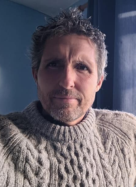 Photo of Kristian Evans. Light is hitting his face from the right and he is wearing a cream knitted jumper.