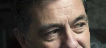 Photo of Paul Henry looking over his shoulder away from the camera. He is wearing a dark leather jacket.