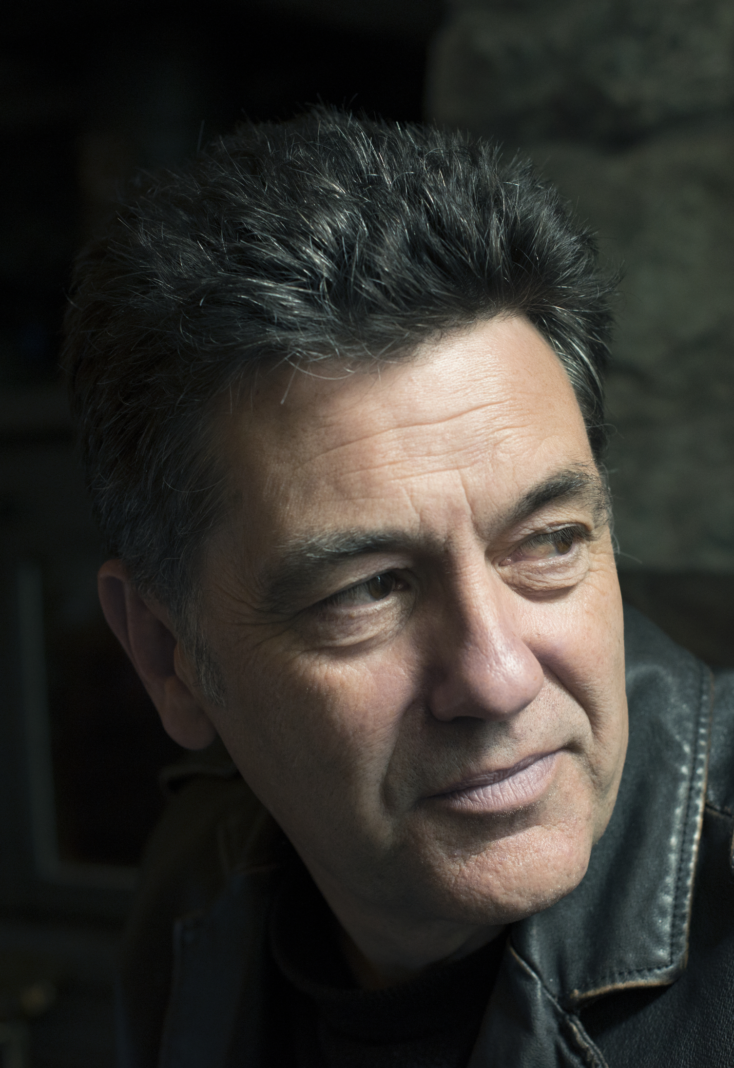Photo of Paul Henry looking over his shoulder away from the camera. He is wearing a dark leather jacket.