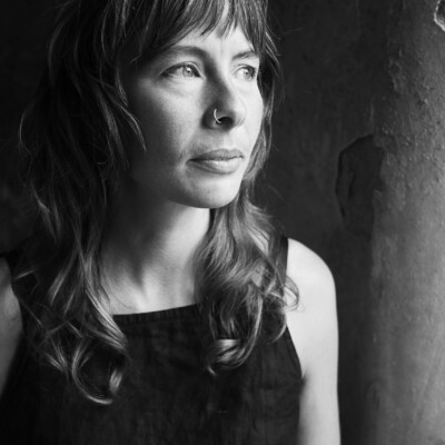 Black and white photo of Sammy Weaver, a white woman with long hair. She is looking away from the camera and light is coming onto her fact from the right hand side.