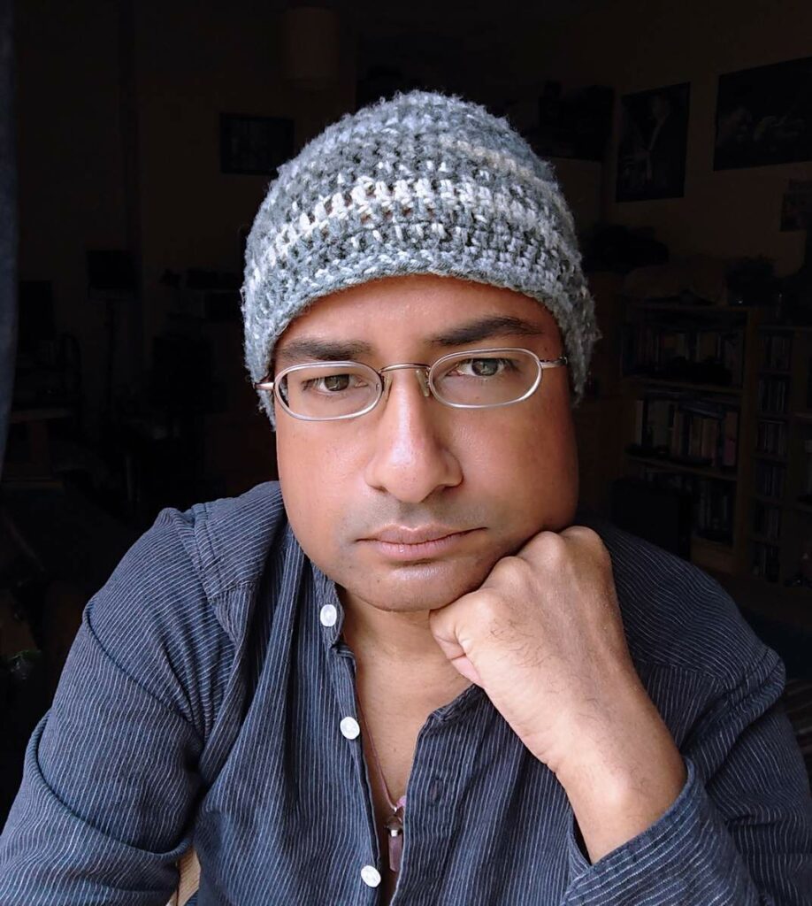 Photo of Taz Rahman wearing a blue shirt and grey beanie hat.