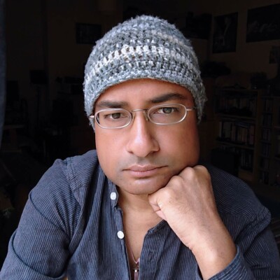 Photo of Taz Rahman wearing a blue shirt and grey beanie hat.