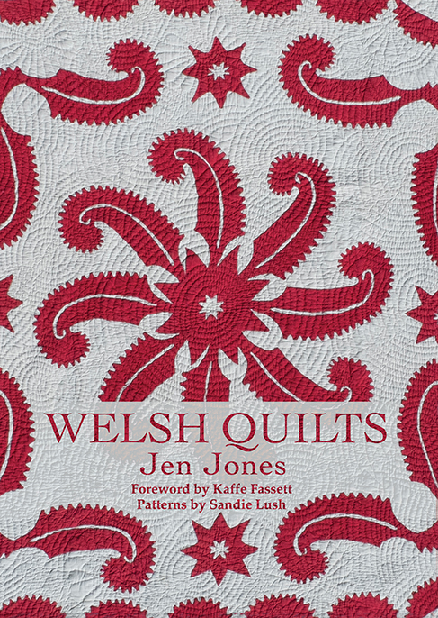 This cover shows a light grey background with a red pattern quilted on. The Text reads: Welsh Quilts. Jen Jones. Foreword by Kaffe Fassett. Patterns by Sandie Lush.