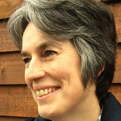 Close up photo of Ilse Pedler standing outside. She is looking slightly away from the camera and is smiling.