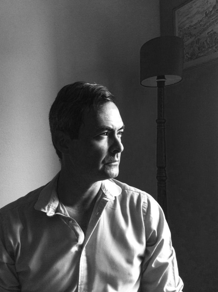 Black and white photo of Damian Walford Davies. He is turned away from the camera and his face is partially in shadow.