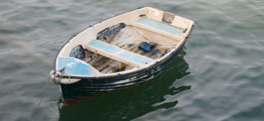 Photo of a small wooden rowing boat drifting along in blue-grey waters.