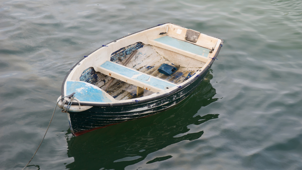 Photo of a small wooden rowing boat drifting along in blue-grey waters.