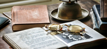 Closeup photograph of an old book, oil lamp and an antique pair of glasses sitting on a desk