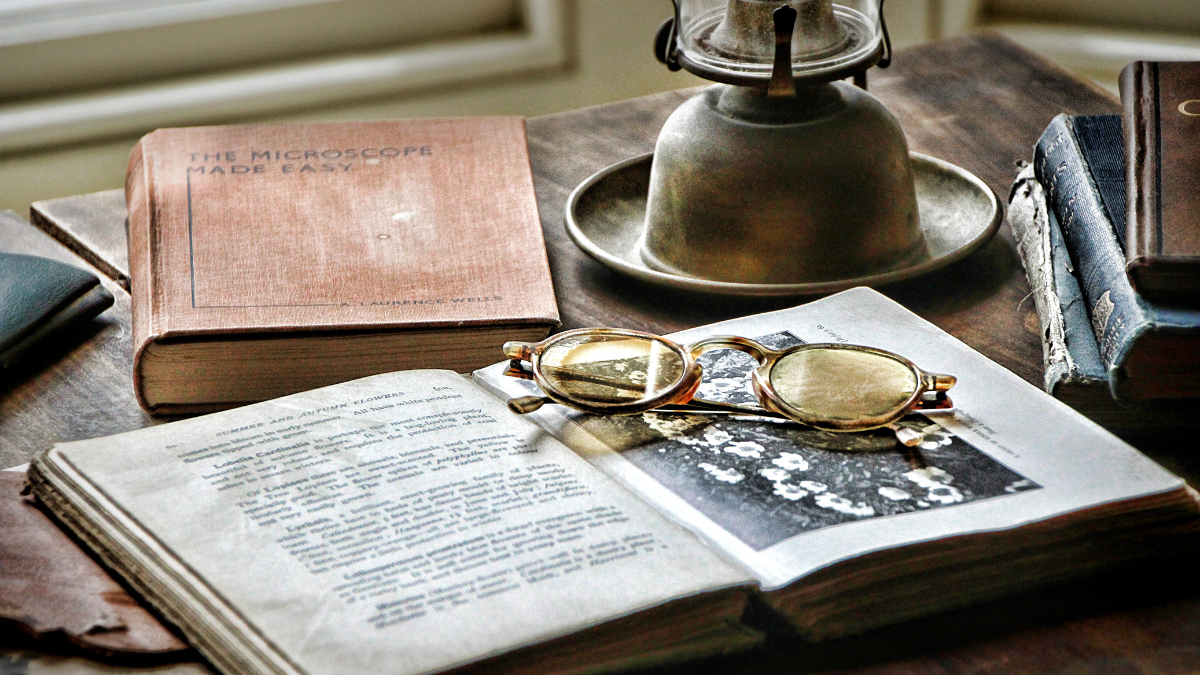 Closeup photograph of an old book, oil lamp and an antique pair of glasses sitting on a desk