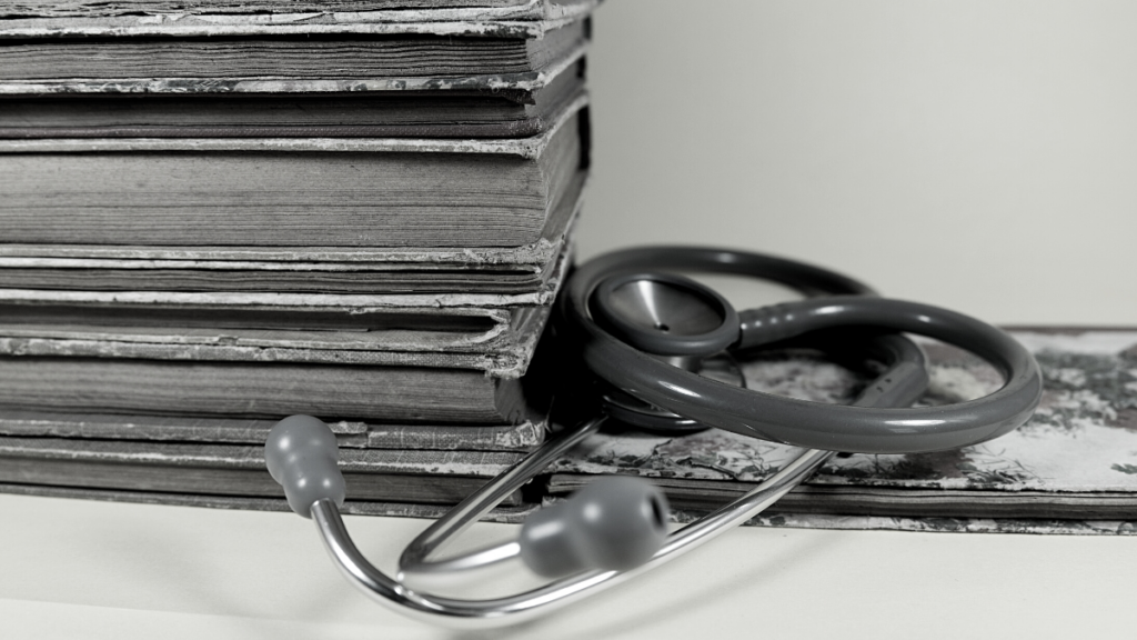 Black and white photo of a stethoscope laying beside a pile of old books.