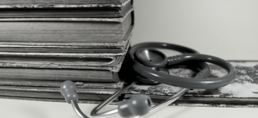 Black and white photo of a stethoscope laying beside a pile of old books.