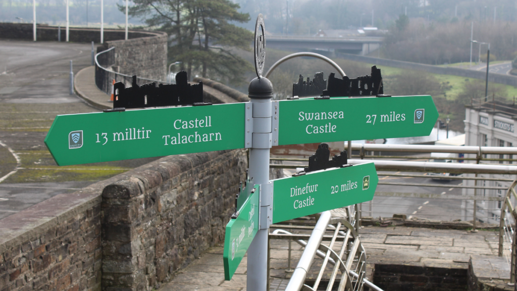 Photograph of a town sign pointing in multiple directions. The grey town is blurred out in the background