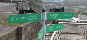 Photograph of a town sign pointing in multiple directions. The grey town is blurred out in the background