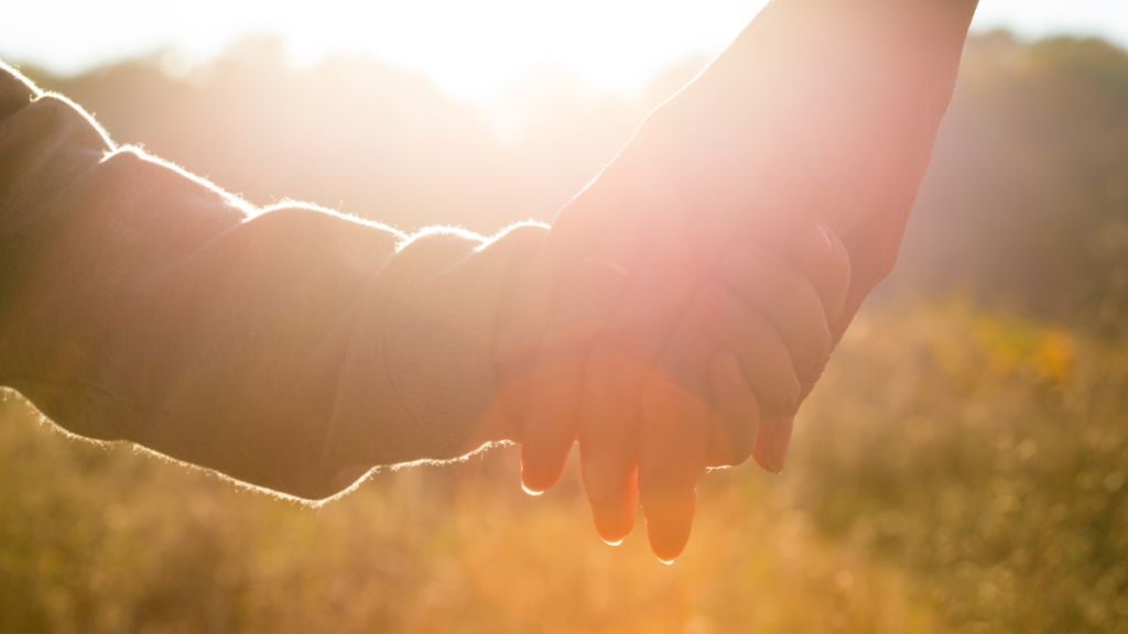 Close up photo of a child's holding onto their parent's hand with the sun flaring over the image.