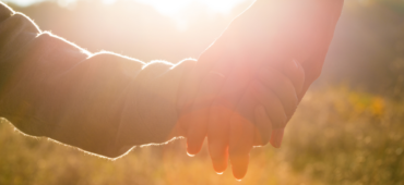 Close up photo of a child's holding onto their parent's hand with the sun flaring over the image.