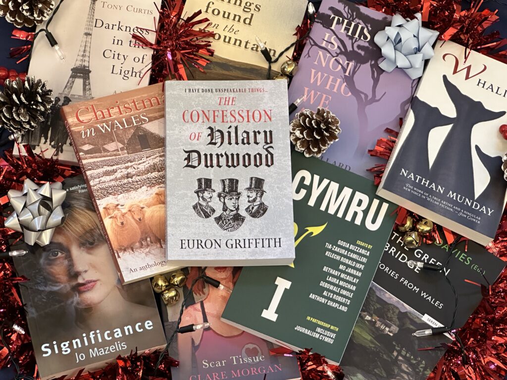 Photograph of lots of Seren non-fiction titles including Christmas in Wales, Cymru and I and The Confession of Hilary Durwood lying in a scattered pile surrounded by festive decorations.