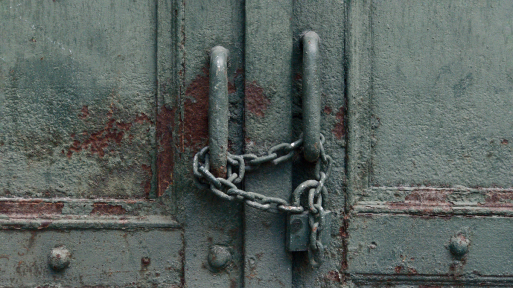 Close up photo of a rusty old door locked with a padlock and chain.