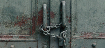 Close up photo of a rusty old door locked with a padlock and chain.