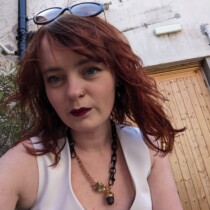 Photo of Emily Cotterill. She is wearing a white top and has shoulder length red hair.