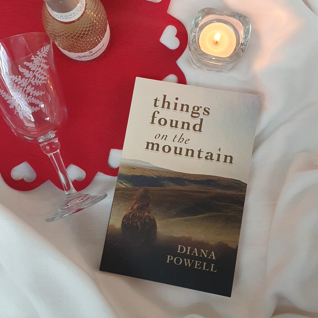 Photograph of Things Found on the Mountain laid out on a blanket with a lit candle and a small bottle of wine