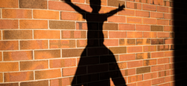 Shadow of a child sitting with their arms and legs outstretched on top of someone's shoulders