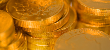 Close up photo of stacked, chocolate coins wrapped in shiny golden foil.