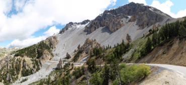 Photo of a dusty road bending to the left and disappearing into rocky mountains