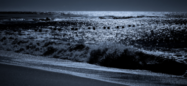 Dark photo of waves rolling into the shore a night time