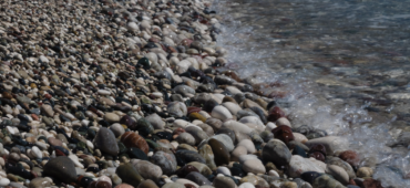 Close up photo of a pebbled shore with waves lapping in from the sea.