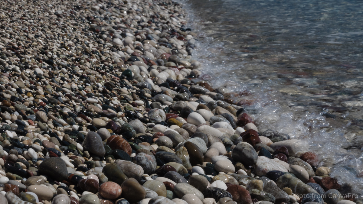Close up photo of a pebbled shore with waves lapping in from the sea.