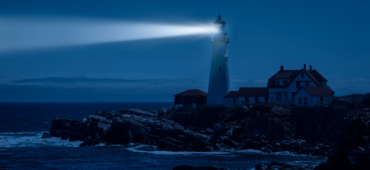 Photo of a light house flashing across the rock in the night.