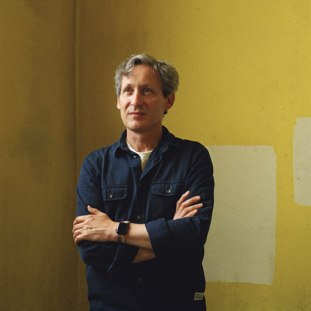 Photo of Richard King. He is standing in a room with yellow walls and his arms are crossed over his body.
