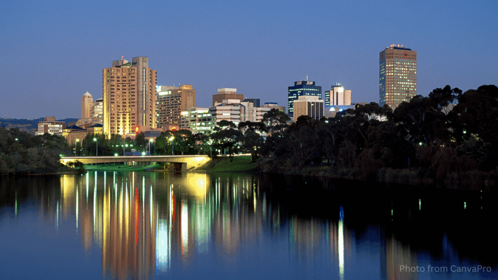 Photo of a city as night falls, its lights streaked in the reflection on the river.