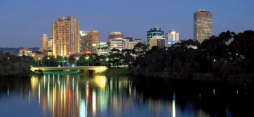 Photo of a city as night falls, its lights streaked in the reflection on the river.