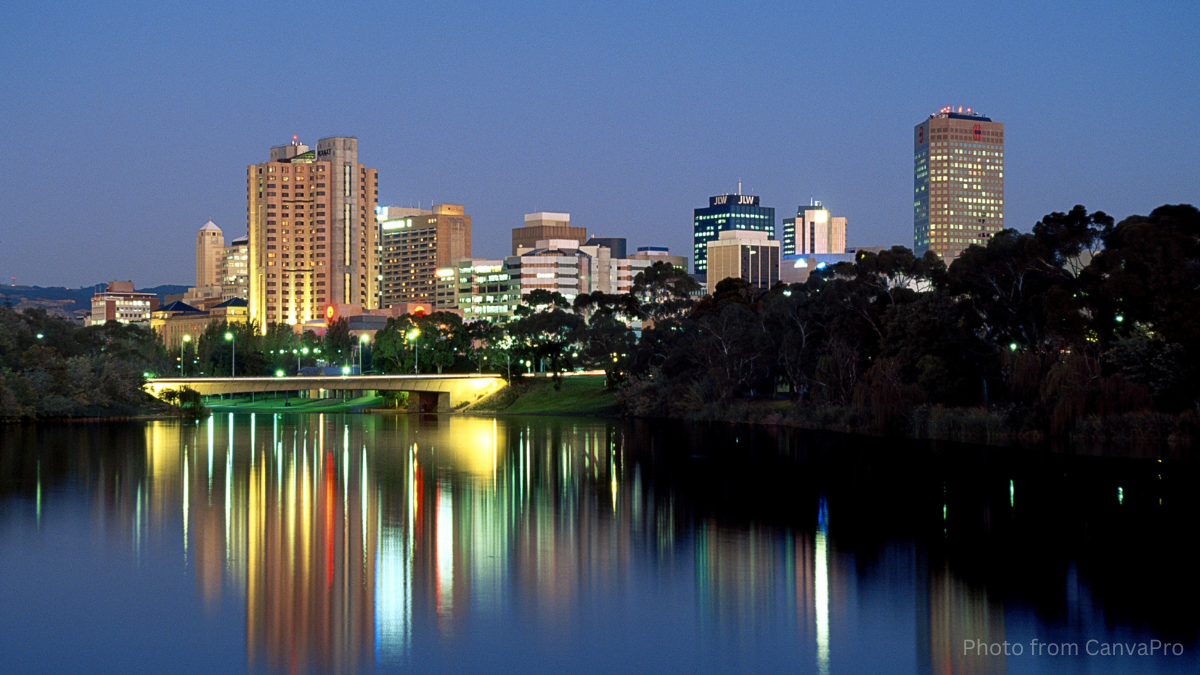 Photo of a city as night falls, its lights streaked in the reflection on the river.