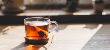 Photo of a steaming cup of tea in a glass mug in the sunlight