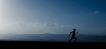 Photo of a lone runner running across a fell as the sun rises over distant mountains.