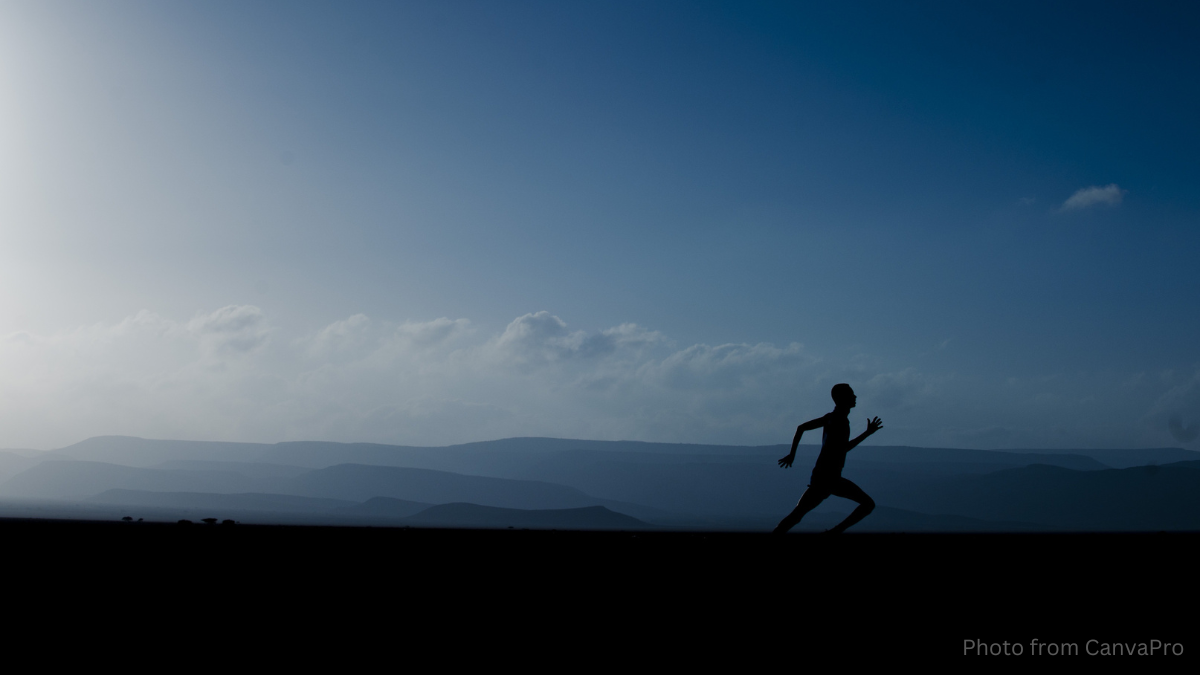 Photo of a lone runner running across a fell as the sun rises over distant mountains.