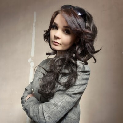 Colour photograph of Natalie Ann Holborow. She is looking purposefully into the camera with her arms crossed and is wearing a grey blazer.