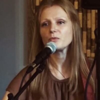 Photo of Laura Wainwright singing at an event. She has long auburn hair and is wearing a brown dress.