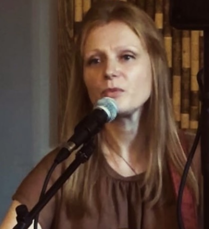 Photo of Laura Wainwright singing at an event. She has long auburn hair and is wearing a brown dress.
